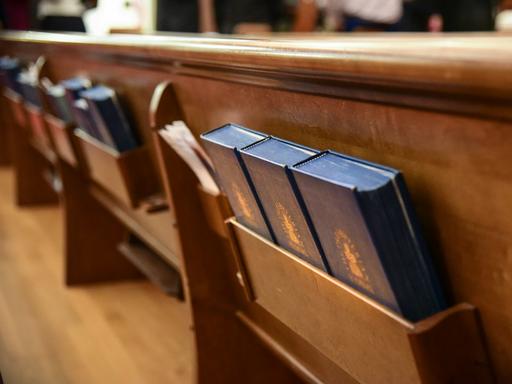 Blick in Kirchenbänken, in denen Gesangsbücher in Fächer aufgeräumt sind.