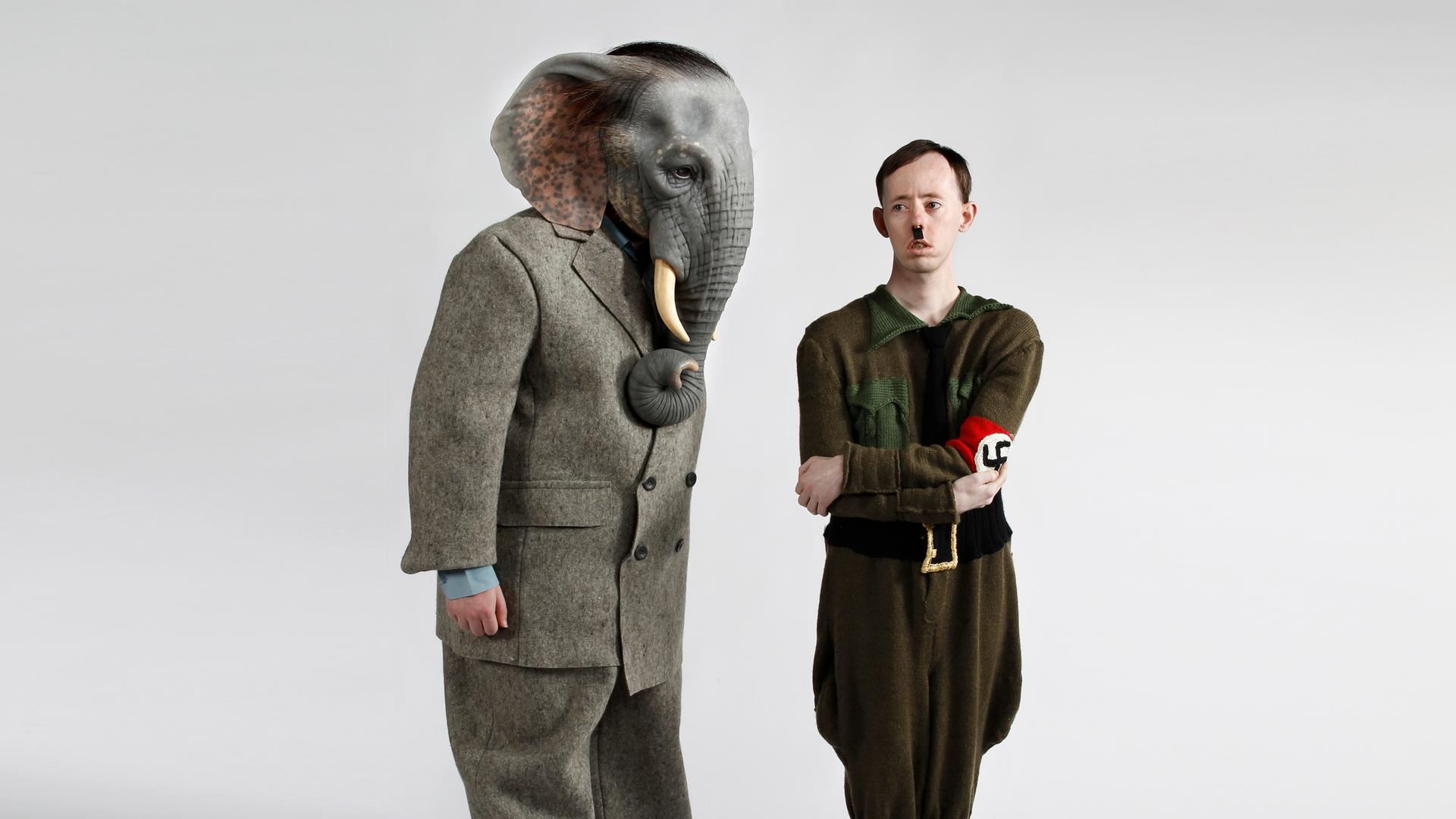 Ein Schauspieler mit einer Elefantenkopfmaske und ein zweiter, der Hitler darstellt, stehen auf einer Bühne.