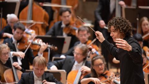 Dirigent Robin Ticciati öffnet seine Arme weit Richtung Orchester.