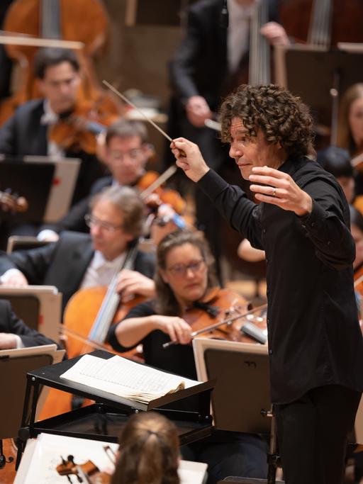 Dirigent Robin Ticciati öffnet seine Arme weit Richtung Orchester.