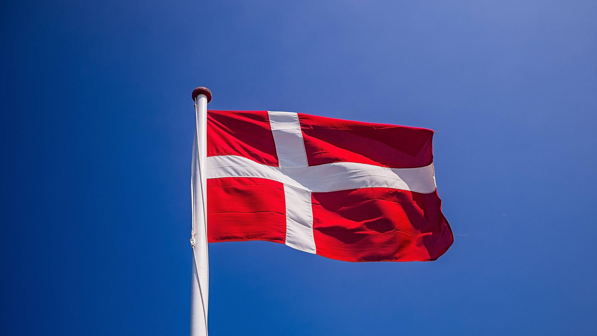 Eine dänische Flagge weht unter blauem Himmel.