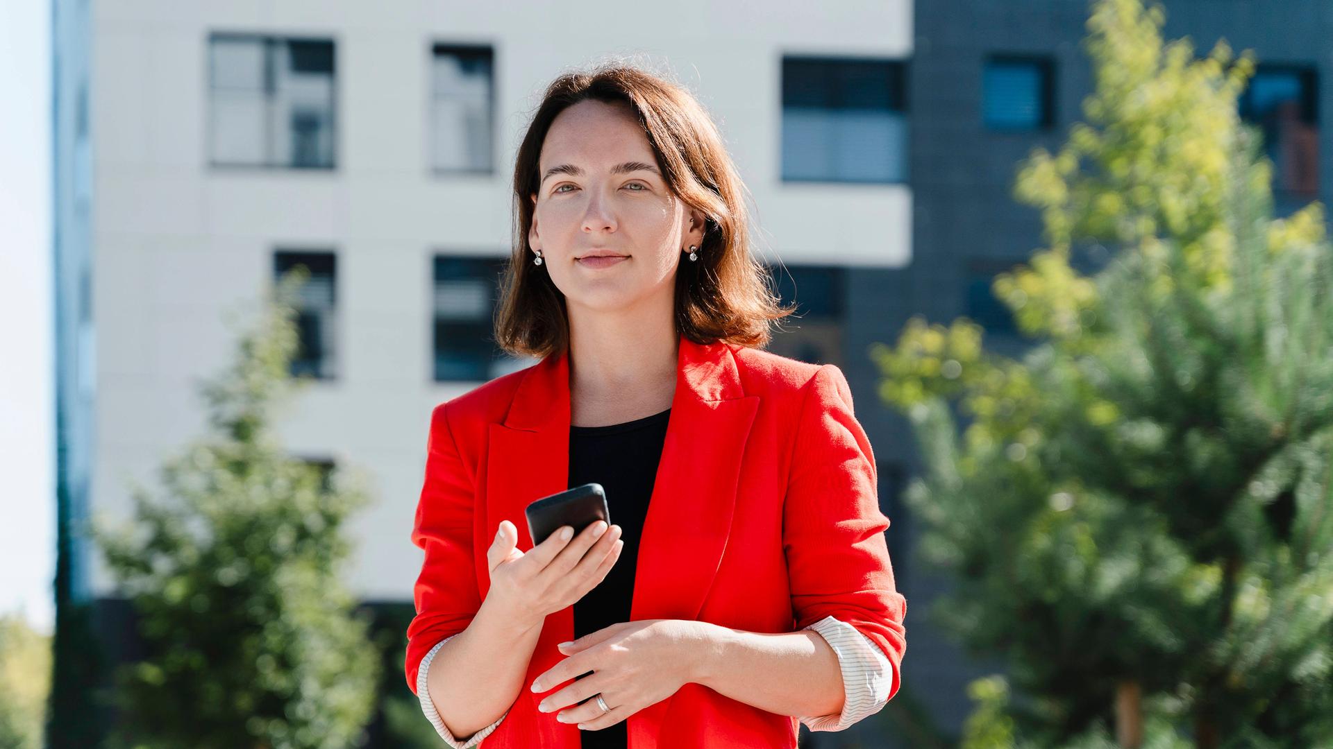 Das Foto zeigt eine Frau in einem roten Blazer und mit einem Handy Das Foto zeigt eine Frau in einem roten Blazer und mit einem Handy