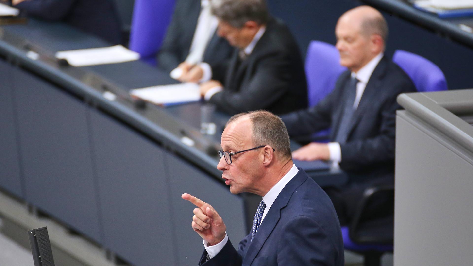 CDU-Chef Friedrich Merz rechts spricht am Tag der Vertrauensfrage im Deutschen Bundestag. Dabei steht er mit erhobenem Zeigefinger am anthrazitfarbenen Rednerpult. Im Hintergrund sitzt Bundeskanzler Scholz auf der Regierungsbank.