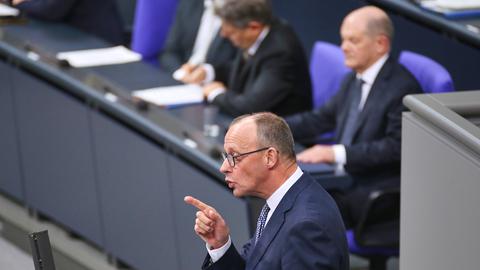 CDU-Chef Friedrich Merz spricht im Deutschen Bundestag. Dabei steht er mit erhobenem Zeigefinger am anthrazitfarbenen Rednerpult. Im Hintergrund sitzt Bundeskanzler Scholz auf der Regierungsbank.