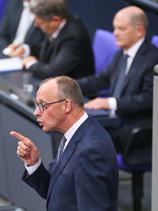 CDU-Chef Friedrich Merz rechts spricht am Tag der Vertrauensfrage im Deutschen Bundestag. Dabei steht er mit erhobenem Zeigefinger am anthrazitfarbenen Rednerpult. Im Hintergrund sitzt Bundeskanzler Scholz auf der Regierungsbank.