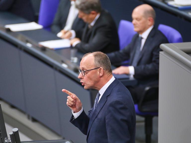 CDU-Chef Friedrich Merz rechts spricht am Tag der Vertrauensfrage im Deutschen Bundestag. Dabei steht er mit erhobenem Zeigefinger am anthrazitfarbenen Rednerpult. Im Hintergrund sitzt Bundeskanzler Scholz auf der Regierungsbank.