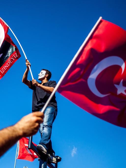 Ein Demonstrant mit Anonymous-Maske und Atatürk-Fahne, davor eine Türkei-Fahne. 