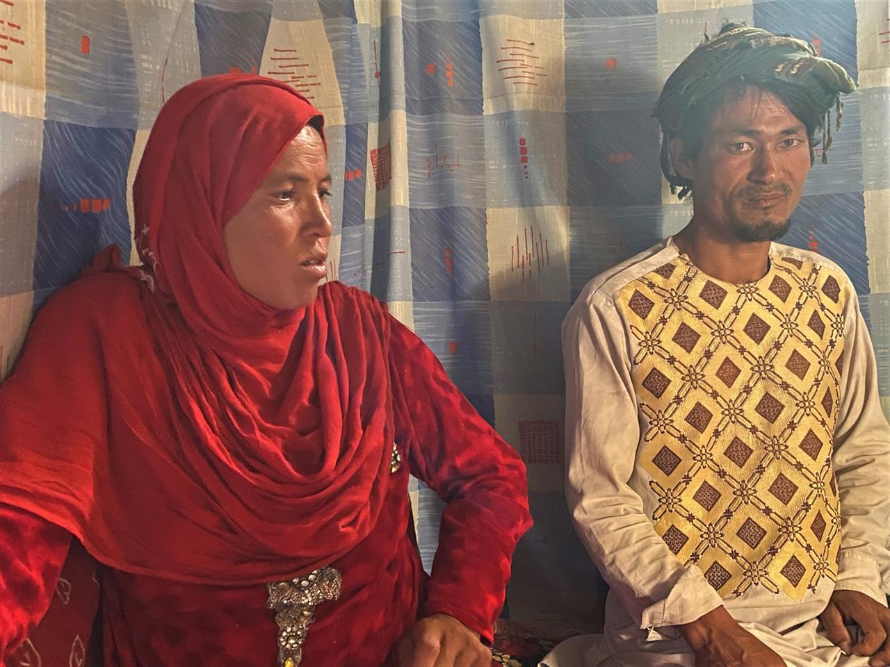 Ein Paar in afghanischer Tracht - sie mit einem roten Tuch über dem Kopf - sitzt nebeinander auf dem Boden.