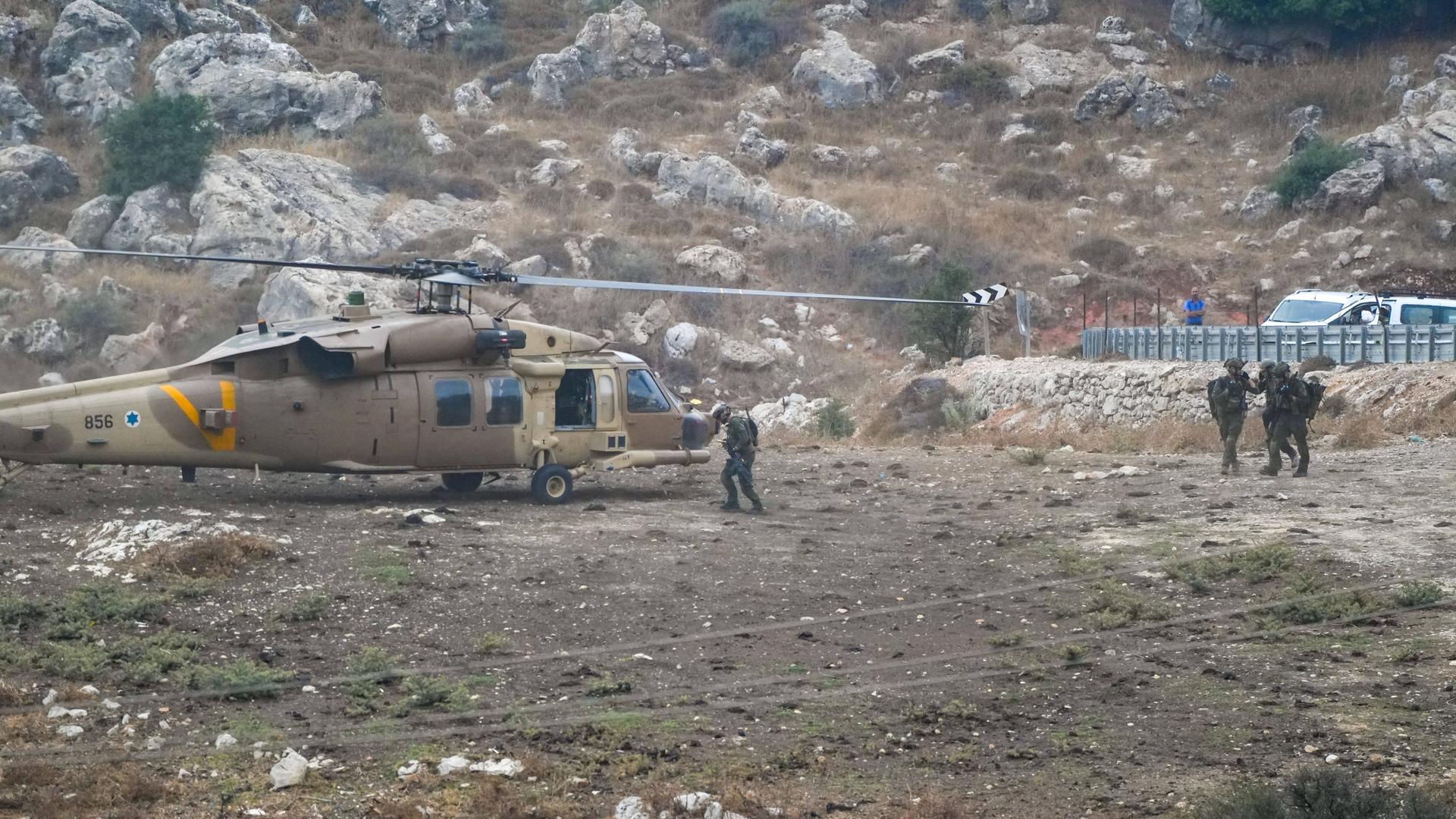Vier Soldaten vor einem Hubschrauber in einer felsigen Landschaft.