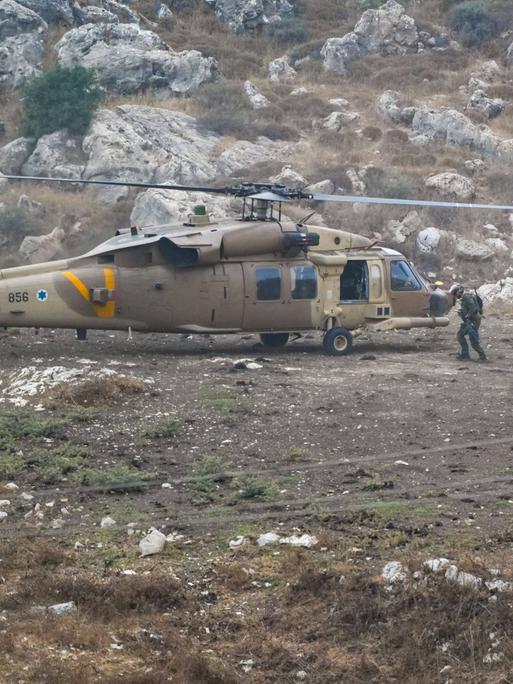 Vier Soldaten vor einem Hubschrauber in einer felsigen Landschaft.