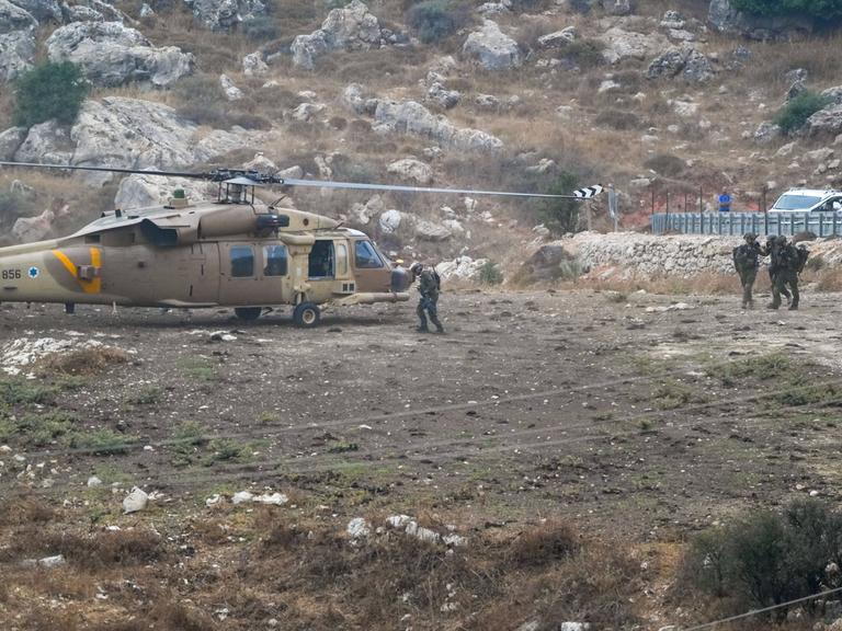 Vier Soldaten vor einem Hubschrauber in einer felsigen Landschaft.