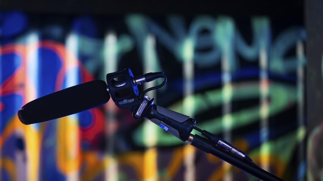 Ein Mikrofon im Vordergrund vor einem bunt beleuchteten Graffiti-Hintergrund in einem Studio, London, England, Großbritannien