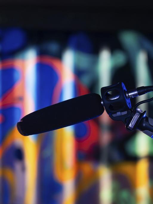 Ein Mikrofon im Vordergrund vor einem bunt beleuchteten Graffiti-Hintergrund in einem Studio, London, England, Großbritannien