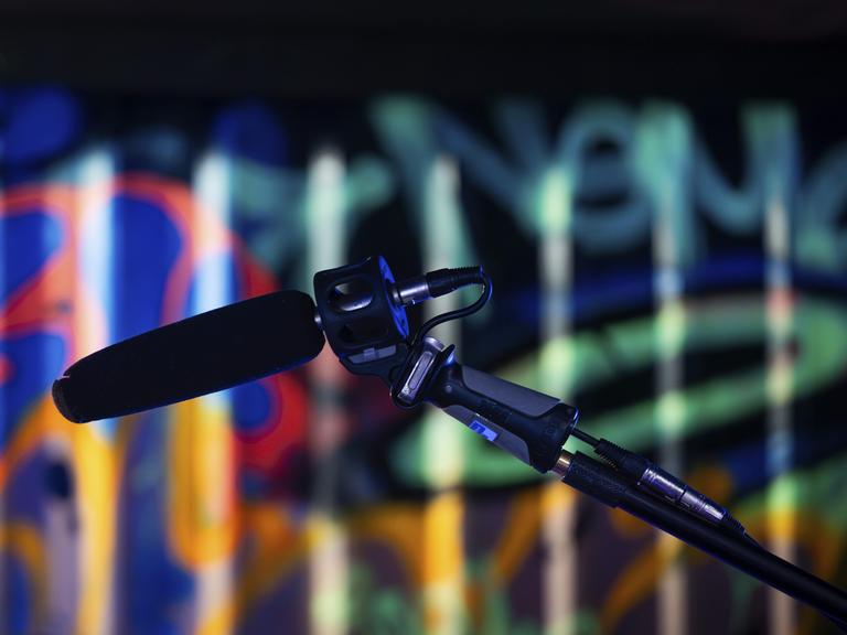 Ein Mikrofon im Vordergrund vor einem bunt beleuchteten Graffiti-Hintergrund in einem Studio, London, England, Großbritannien