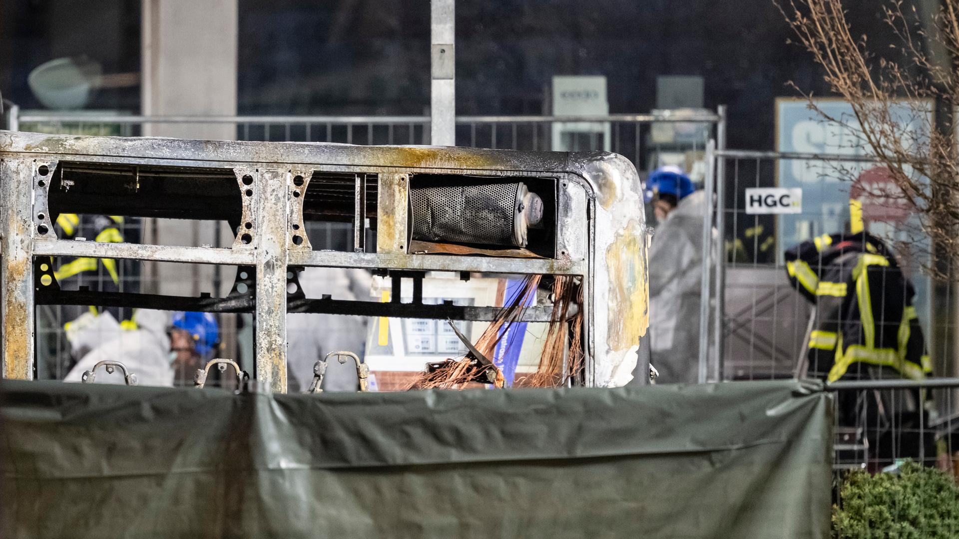 Man sieht die obere Hälfte des ausgebrannten Busses, der untere Teil ist mit einer Plane abgedeckt.