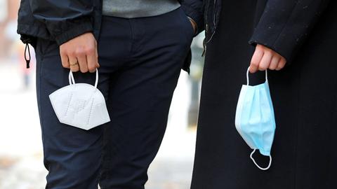 Zwei dunkel gekleidete Menschen halten je eine Maske in der Hand