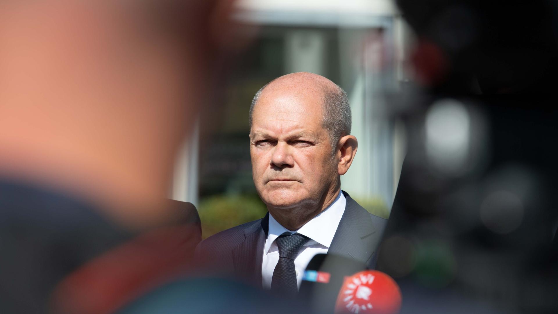 Aufnahme von Bundeskanzler Olaf Scholz, im Vordergrund unscharfe Umrisse vor ihm stehender Personen.