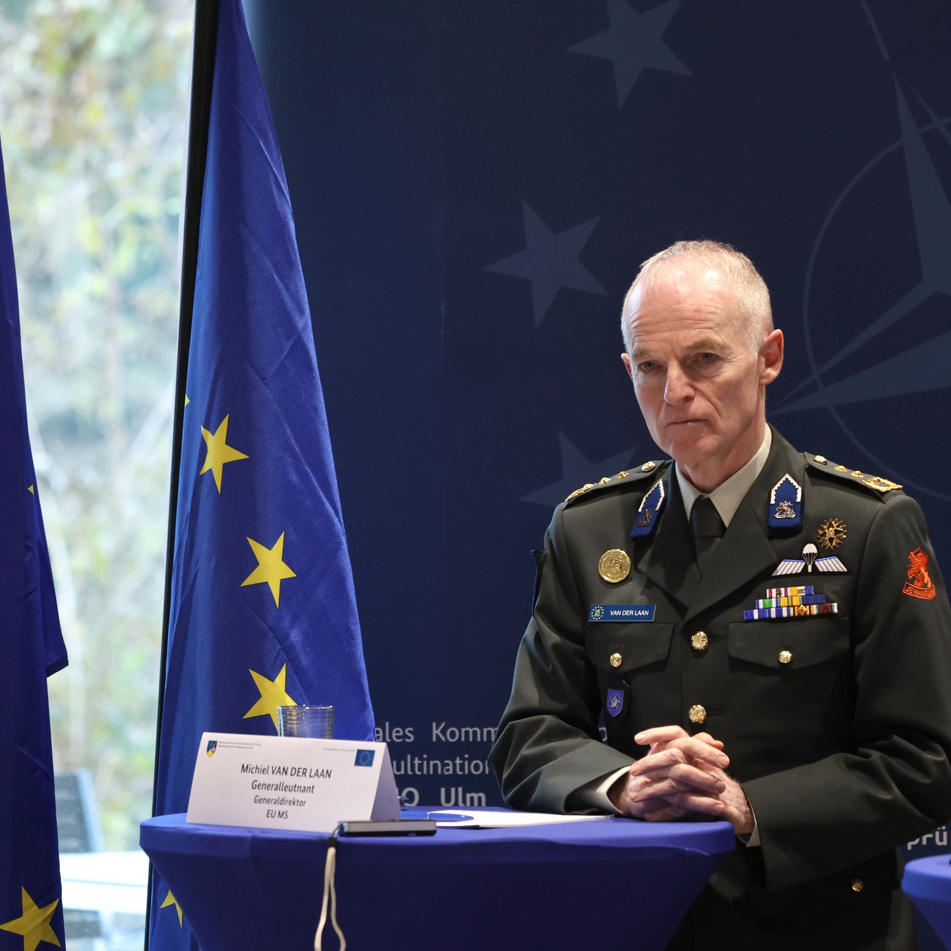 Der niederländische Generalleutnant Michiel van der Laan steht ernst an einem Rednerpult. Seine Hände sind ineinander verschränkt, hinter ihm sind drei EU-Flaggen. 