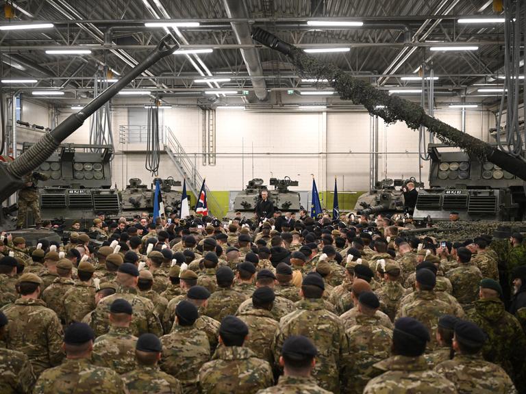 Jens Stoltenberg spricht vor Nato-Truppen in der Tapa Militärbasis. Die Zielfernrohre zweier Panzer rahmen das Bild.