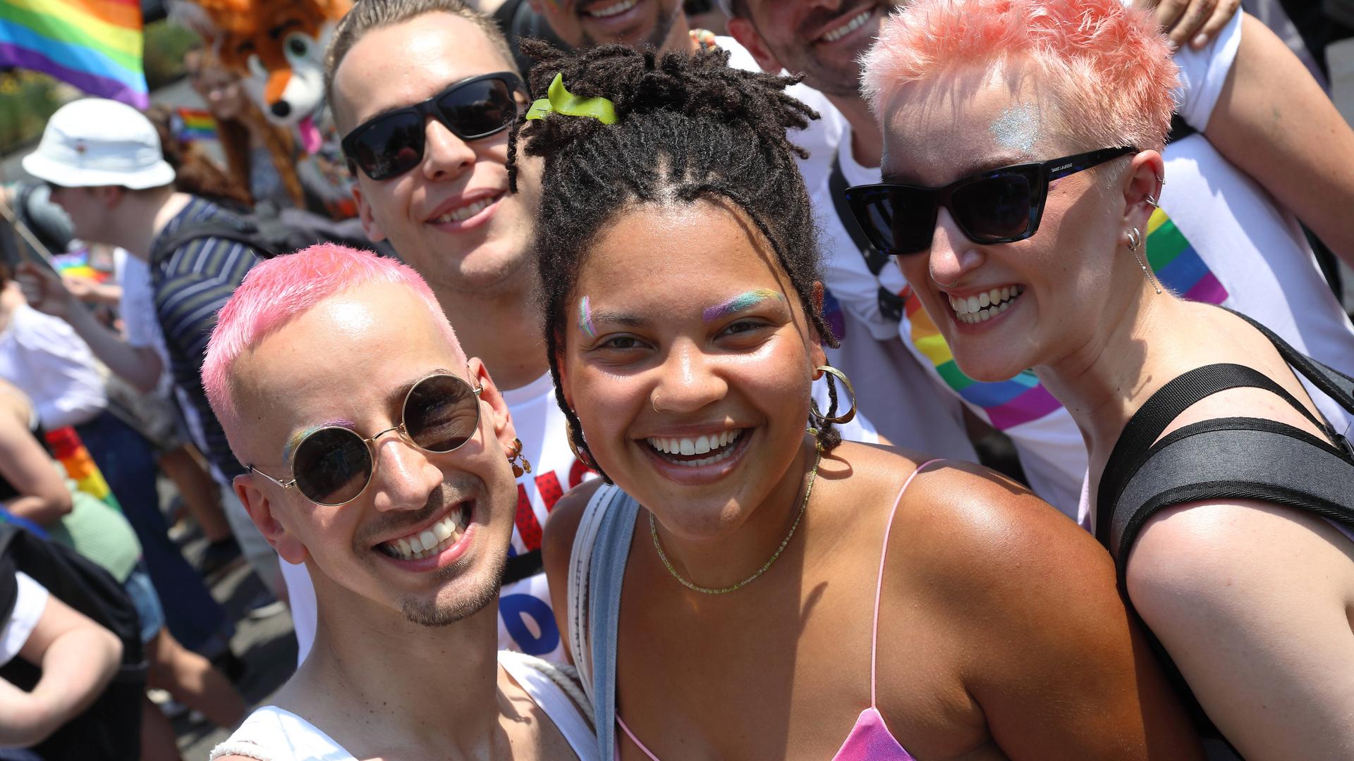 Auf dem Bild posiert eine Gruppe von queeren Menschen für ein Foto. Sie lachen und schauen in Richtung der Kamera. Auf dem Bild posiert eine Gruppe von queeren Menschen für ein Foto. Sie lachen und schauen in Richtung der Kamera.