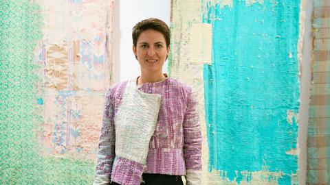 Die deutsche Architektin Anna Heringer steht vor zwei Wandteppichen bei einer Ausstellung