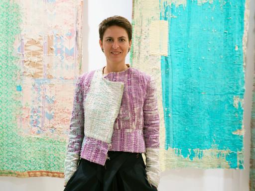 Die deutsche Architektin Anna Heringer steht vor zwei Wandteppichen bei einer Ausstellung