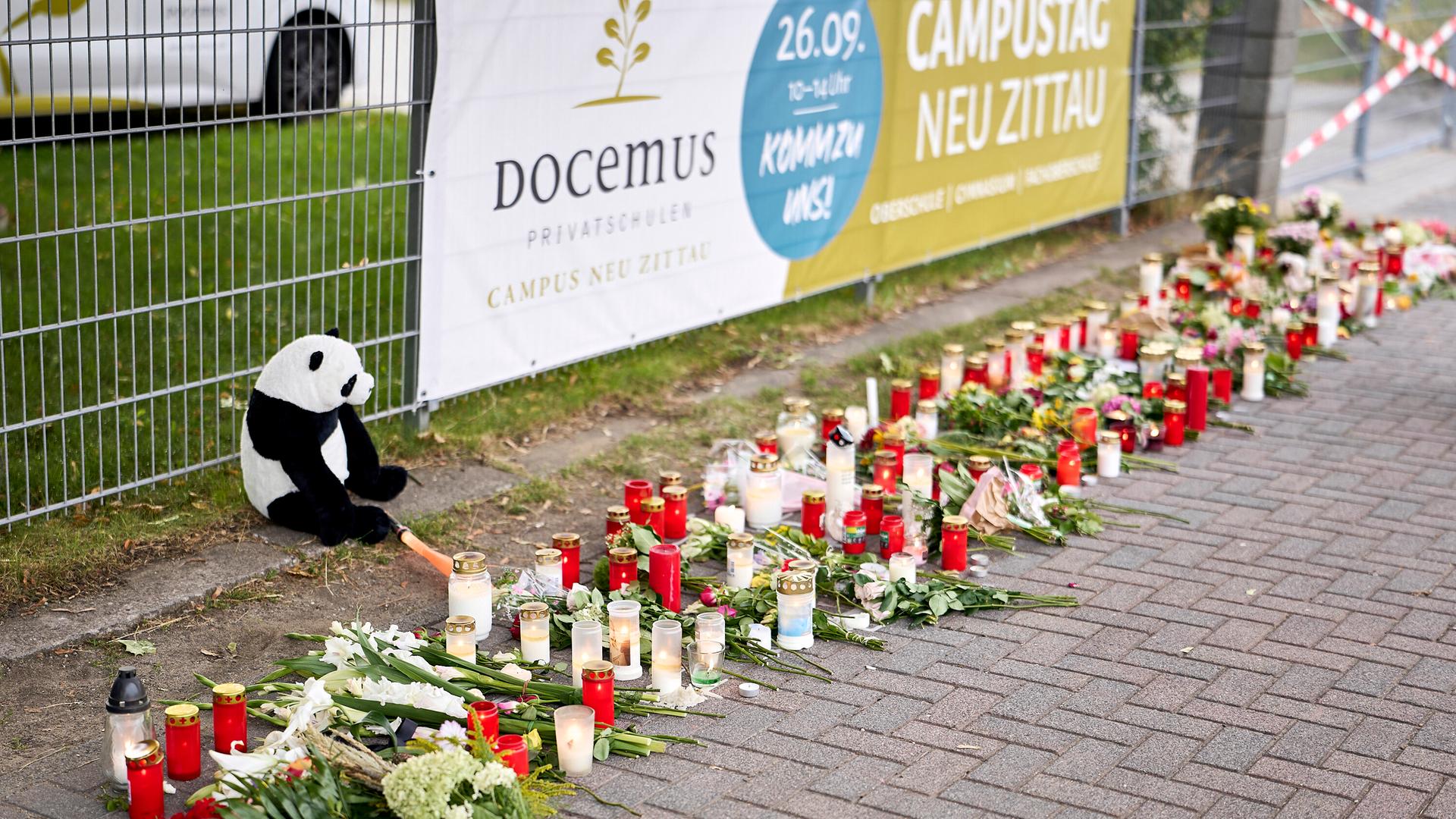 Menschen bringen Blumen und Kerzen zum Gedenken an die Opfer zum Eingang einer Schule in Gosen-Neu Zittau. 