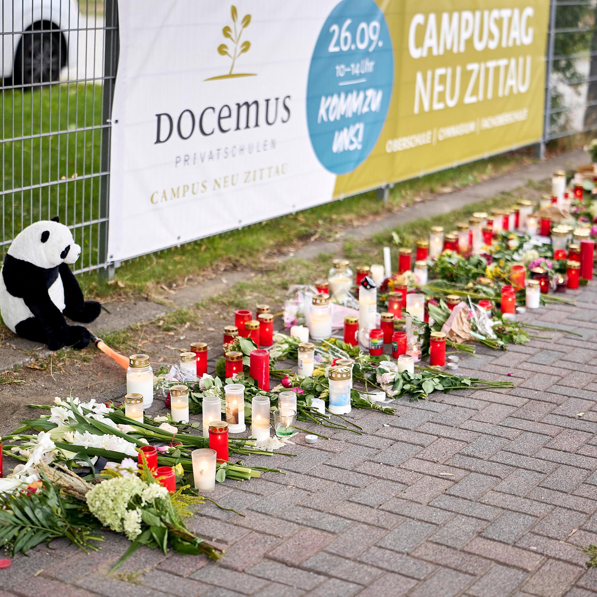 Menschen bringen Blumen und Kerzen zum Gedenken an die Opfer zum Eingang einer Schule in Gosen-Neu Zittau.