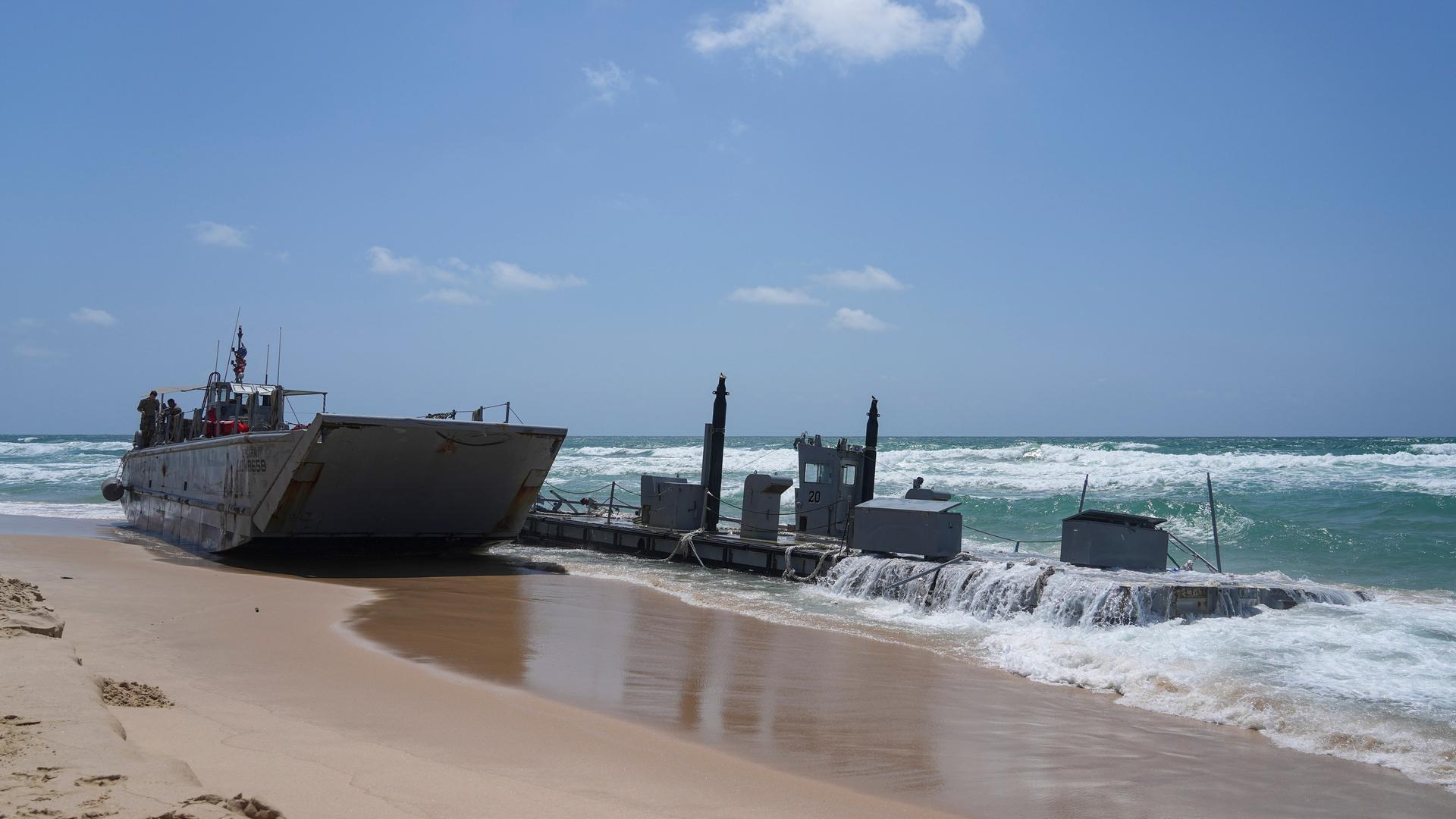 Ein angeschwemmtes Schiff der US-Armee und ein Stück der beschädigten Anlegestelle sind am Strand zu sehen. 