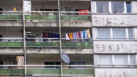 Zu sehen ist die stark verdreckte Fassade eines Hochhauses. Auf den heruntergekommenen Balkonen sind Schrottgegenstände gestapelt. Teilweise ist Wäsche schief aufgehängt. 