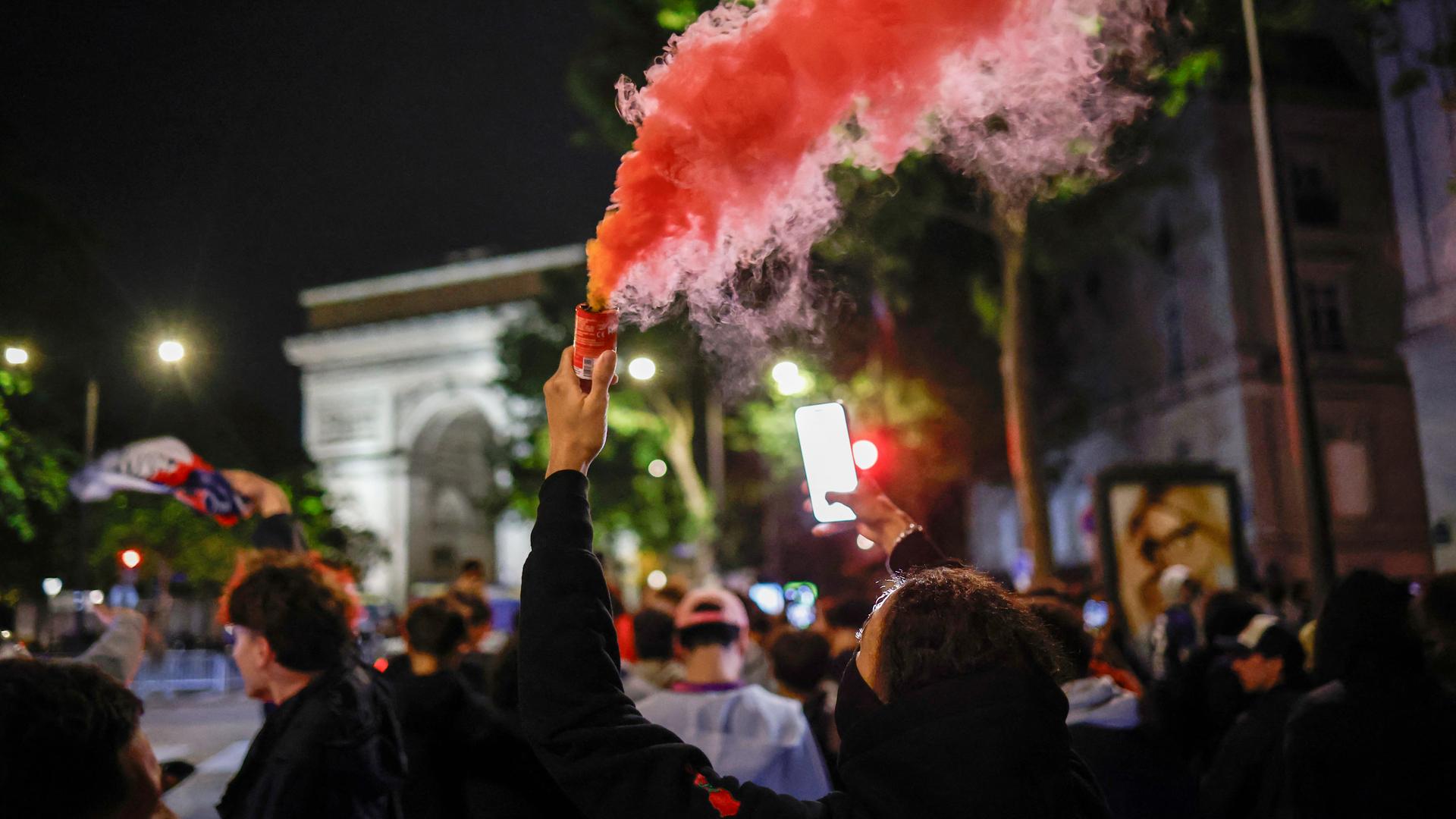 Fans des Vereins Paris Saint-Germain stehen am Triumphbogen in Paris. Ein Fan ist vermummt und zündet Pyrotechnik.
