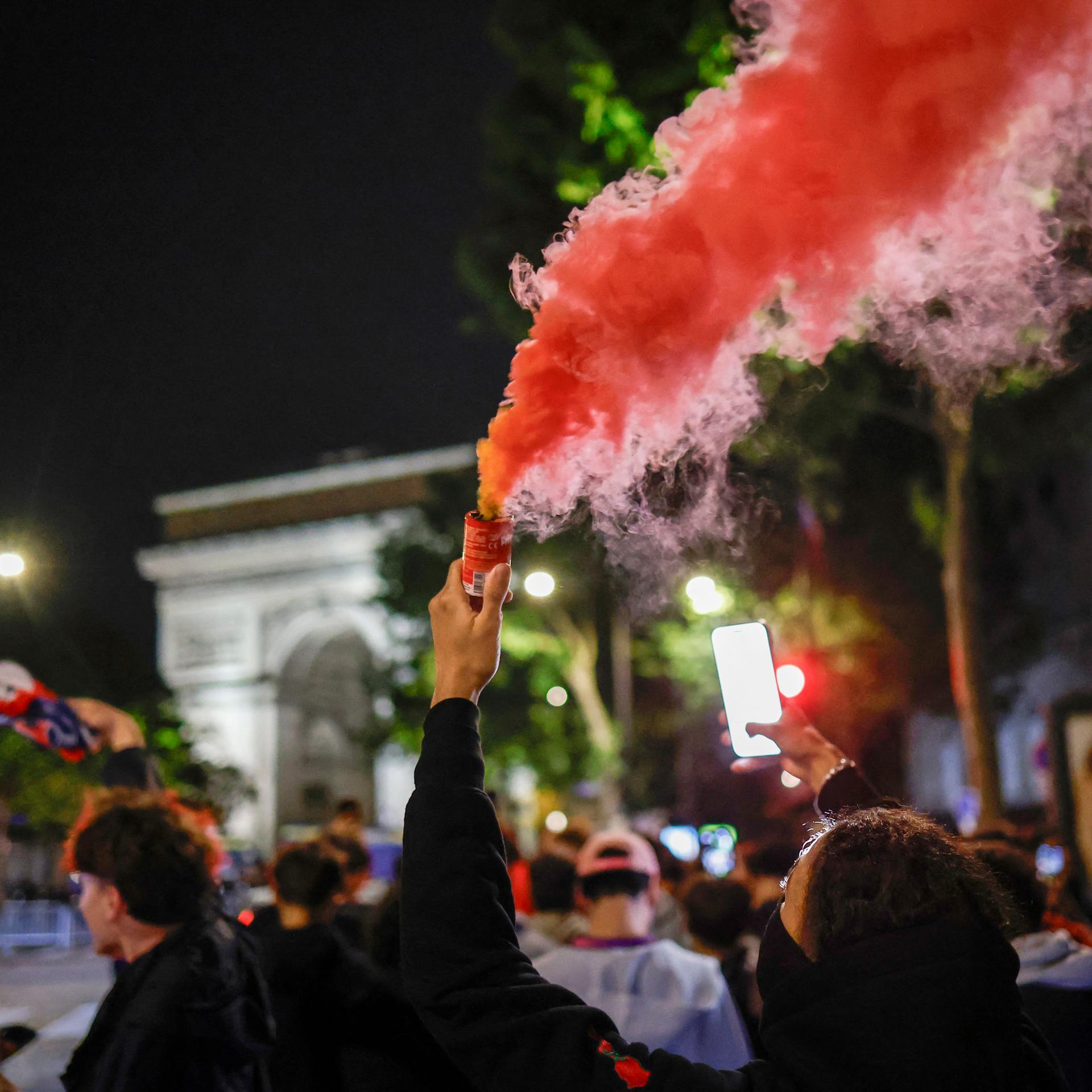 Fans des Vereins Paris Saint-Germain stehen am Triumphbogen in Paris. Ein Fan ist vermummt und zündet Pyrotechnik.