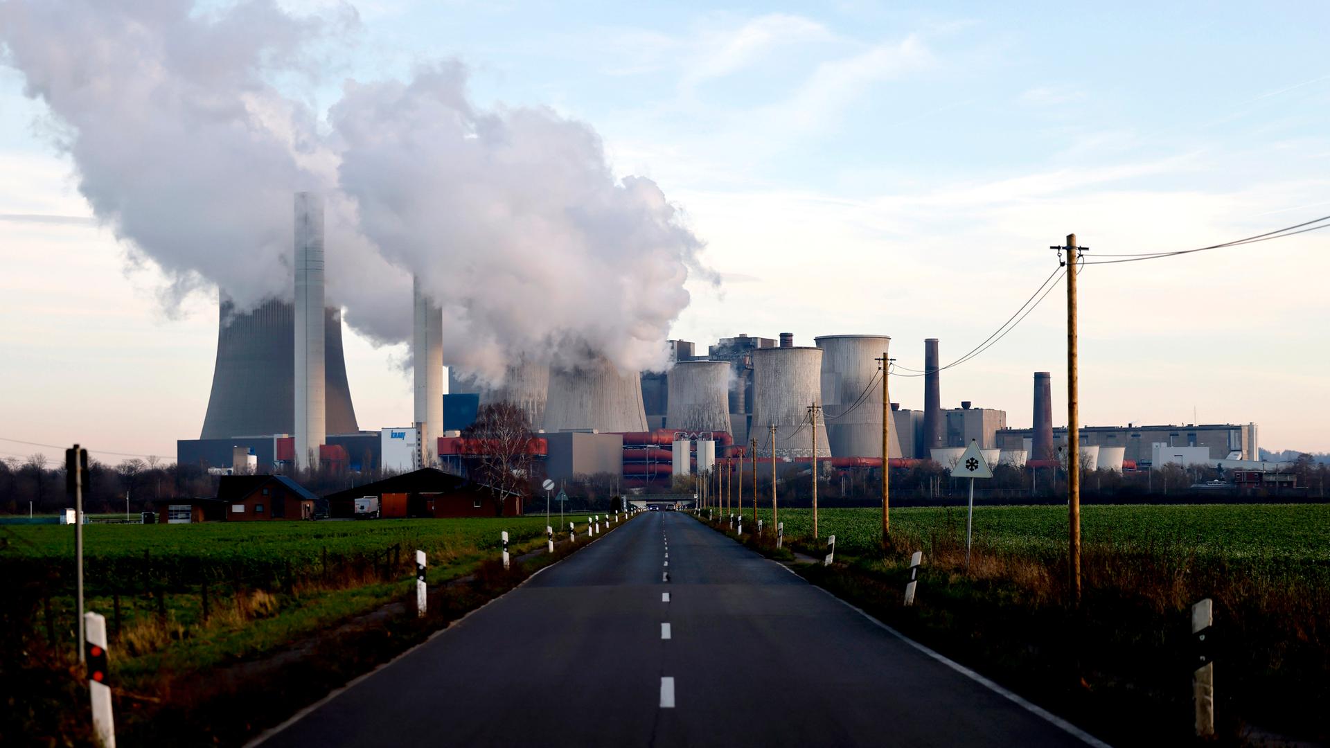 Strommasten um das Kohlekraftwerk Niederaußem des Stromkonzerns RWE. Aus dem Kraftwerk strömt eine dicke graue Wolke. (Symbolbild)