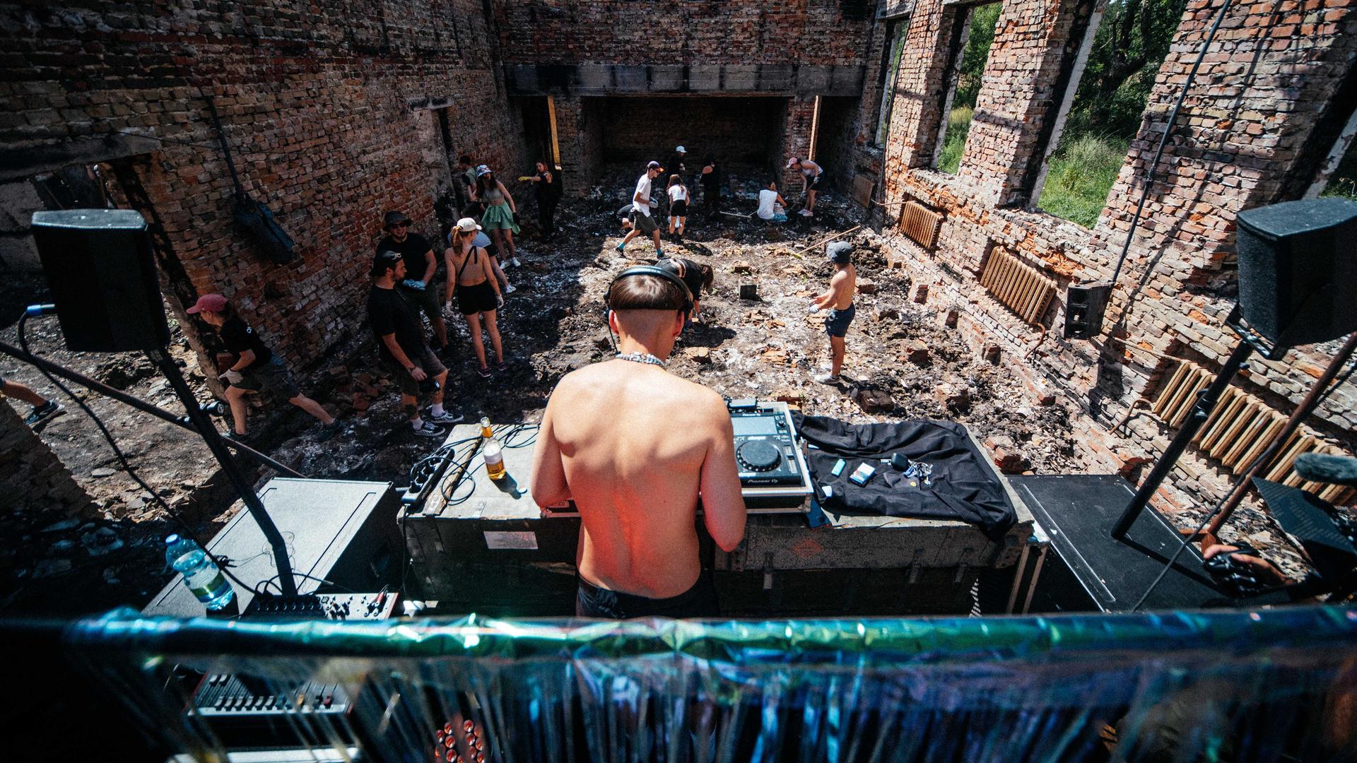 Ein DJ spielt in einer Ruine ohne Dach. Menschen tanzen zwischen den Ziegelsteinwänden.