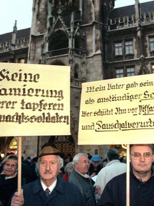 Menschen demonstrieren im Jahr 1997 gegen die damals umstrittene Wehrmachtsausstellung. Einer von ihnen hält ein Plakat mit der Aufschrift: "Keine Diffamierung unserer tapferen Wehrmachtssoldaten"