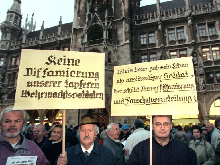 Menschen demonstrieren im Jahr 1997 gegen die damals umstrittene Wehrmachtsausstellung. Einer von ihnen hält ein Plakat mit der Aufschrift: "Keine Diffamierung unserer tapferen Wehrmachtssoldaten"