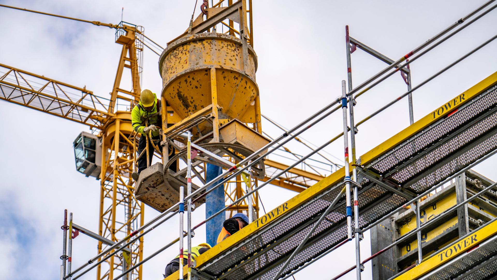 Bauarbeiter betonieren auf einer Baustelle auf einem Gerüst stehend.