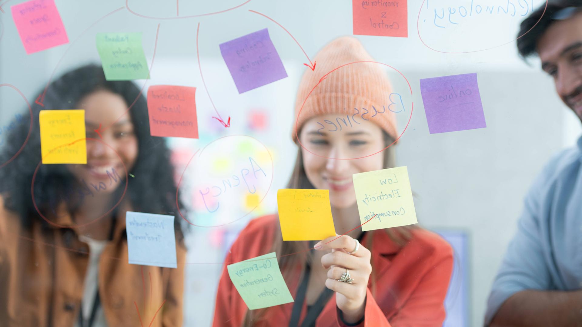 Ein Team von jungen Menschen, die Post-its auf einem transparenten Board anschauen. 