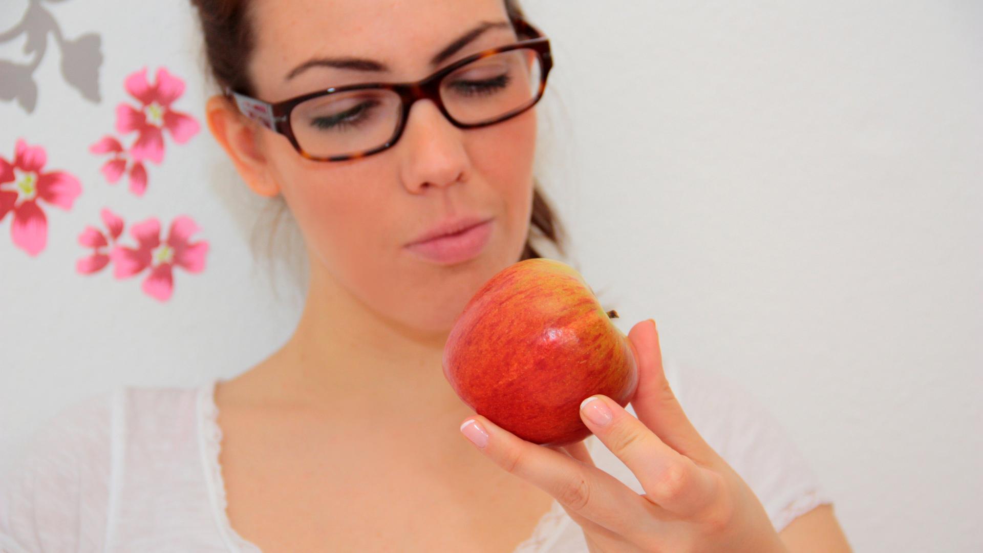 Es gibt Menschen, die bekommen Juck-Reiz oder Schwellungen im Mund, wenn sie einen Apfel essen.. Das Foto zeigt eine junge Frau, die auf einen roten Apfel schaut.