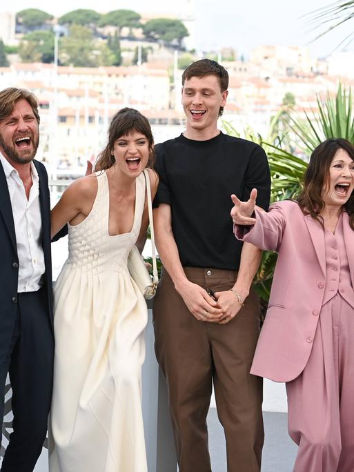 Männer und Frauen des Filmteams bewegen sich fröhlich schreiend in einer Reihe auf die Kameras in Cannes zu.