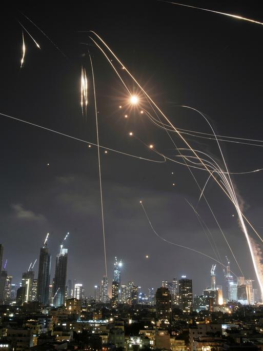 Nachtpanorama mit Skyline von Tel Aviv. Über den Hochhäusen sind iranische Raketen und Gegenraketen der israelischen Abwehr zu sehen