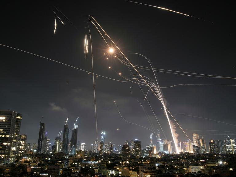Nachtpanorama mit Skyline von Tel Aviv. Über den Hochhäusen sind iranische Raketen und Gegenraketen der israelischen Abwehr zu sehen