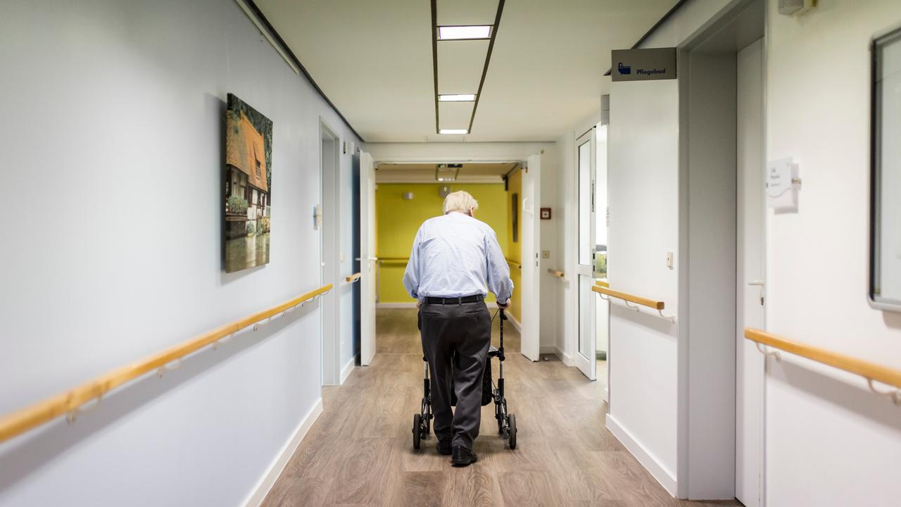 Ein alter Mann läuft mit einem Rollator im Gang einer Pflegeeinrichtung