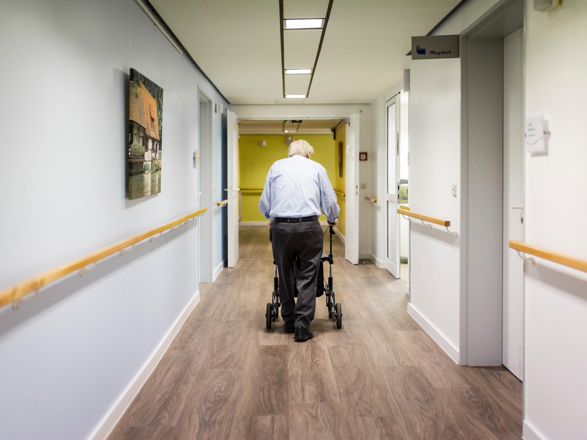Ein alter Mann läuft mit einem Rollator im Gang einer Pflegeeinrichtung