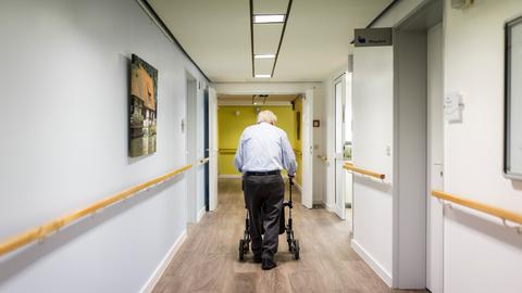 Ein alter Mann läuft mit einem Rollator im Gang einer Pflegeeinrichtung