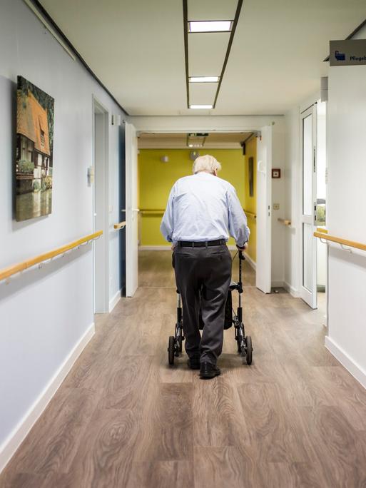 Ein alter Mann läuft mit einem Rollator im Gang einer Pflegeeinrichtung