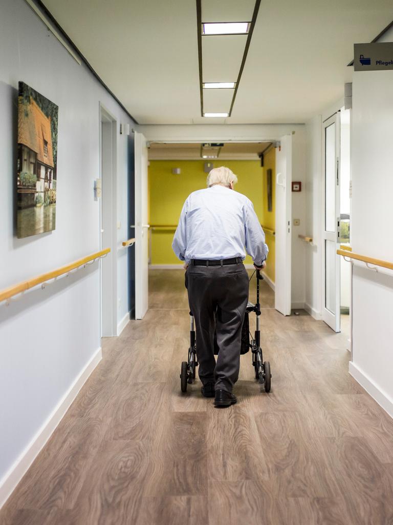 Ein alter Mann läuft mit einem Rollator im Gang einer Pflegeeinrichtung