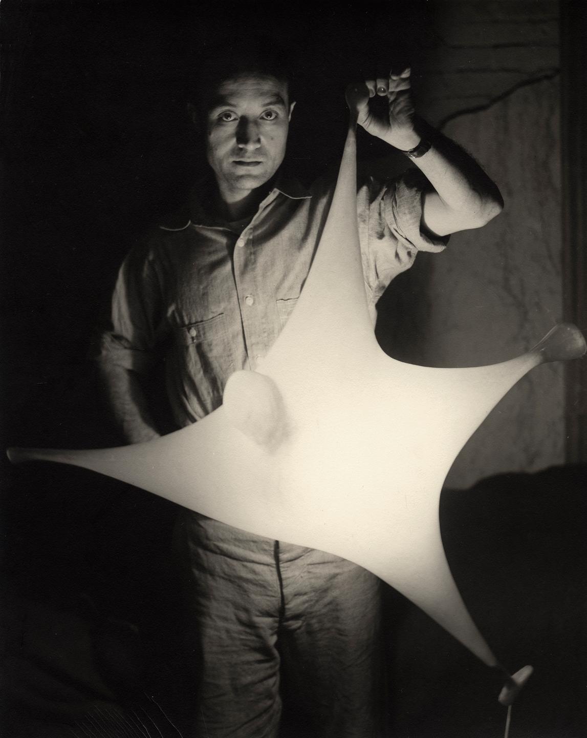 Schwarzweißfoto von Isamu Noguchi, eine leuchende Skulptur haltend. Schwarzweißfoto von Isamu Noguchi, eine leuchende Skulptur haltend.