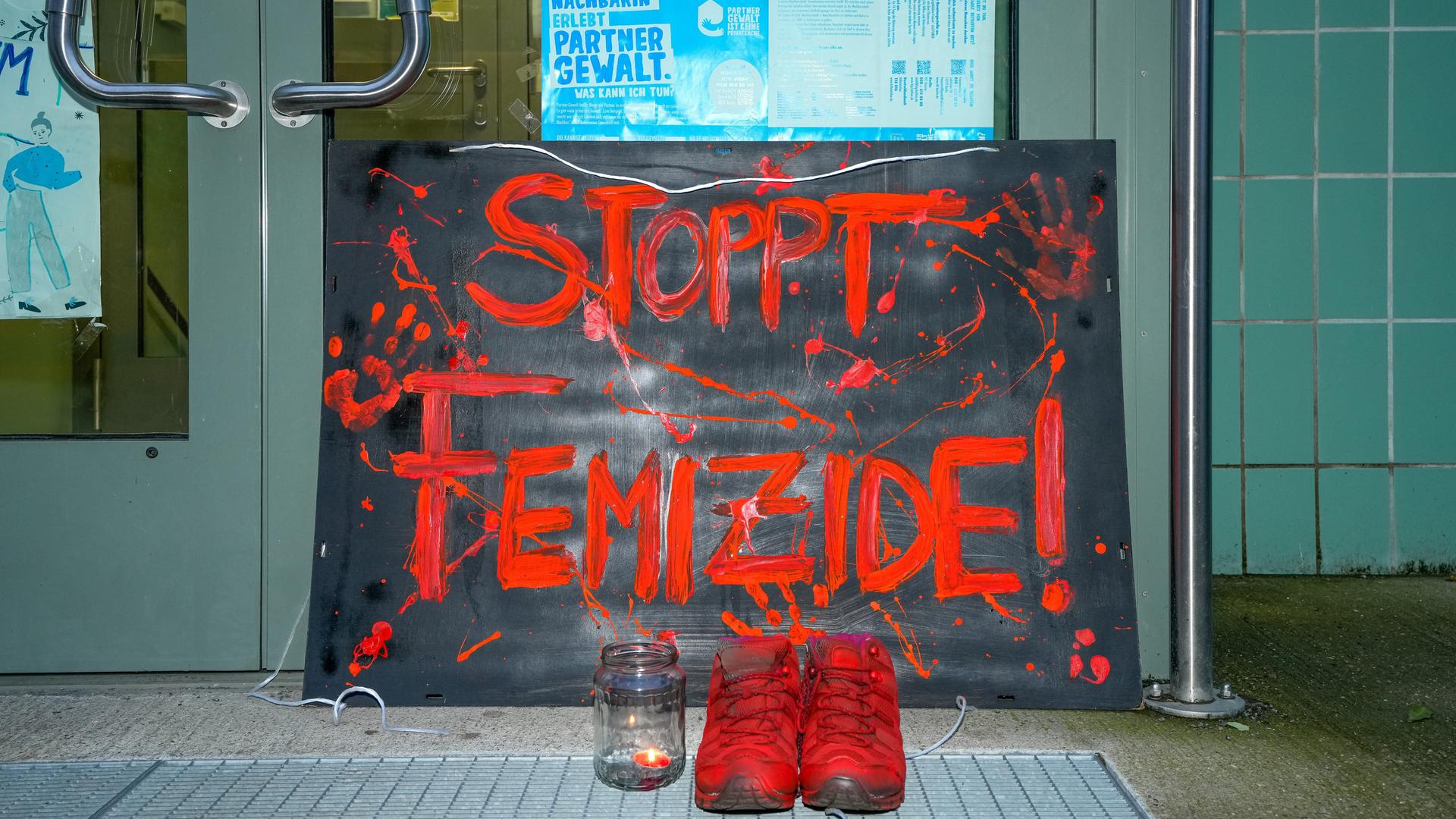 Vor der Eingangstür des Mädchenzentrums Szenenwechsel in Neukölln steht ein Schild mit der Aufschrift "STOPPT FEMIZIDE!". Dazu steht ein paar Schuhe in Orange und ein Teelicht mit brennender Kerze.