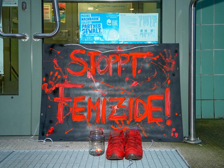 Vor der Eingangstür des Mädchenzentrums Szenenwechsel in Neukölln steht ein Schild mit der Aufschrift "STOPPT FEMIZIDE!". Dazu steht ein paar Schuhe in Orange und ein Teelicht mit brennender Kerze.